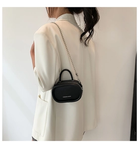 Close-up of mini black lychee leather pill-shaped bag with silver chain and white text