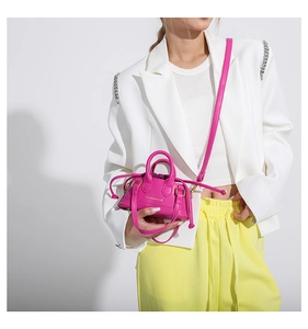 Close-up of fuchsia mini crossbody bag with gold text on a stylish white blazer