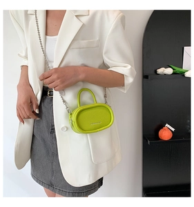 Detailed view of mini green lychee leather handbag with silver chain on a white blazer