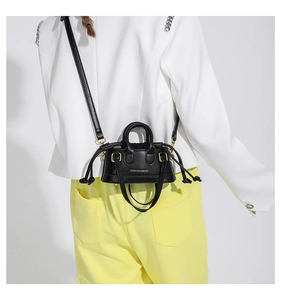 Detail of mini black crossbody bag with gold hardware and fashion print on a model