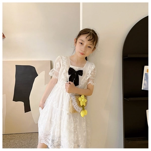 Detail of a girl wearing a white lace dress with a black bow and straw crossbody bag