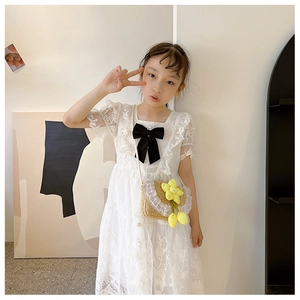 Close-up of white girls lace dress with black satin bow and floral straw bag