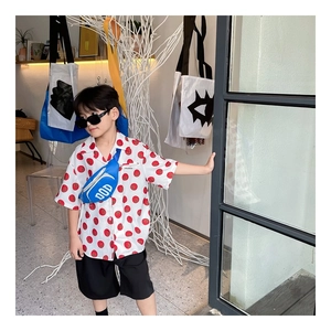 Detail view of cotton shirt with tomato print, black shorts, and blue crossbody bag
