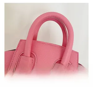 Close-up of pink litchi grain leather handle and stitching detail on small handbag