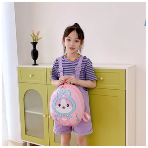 Pink cartoon rabbit egg-shaped backpack shown on a child model in a home setting