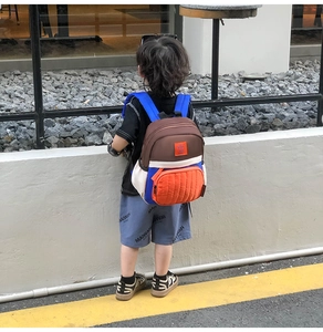 Outdoor shot of a colorful kids backpack with blue straps and an orange quilted front pocket