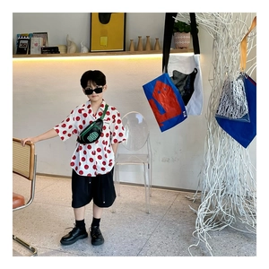 Detail showing kids green crossbody chest bag with DOD logo and trendy red polka dot shirt
