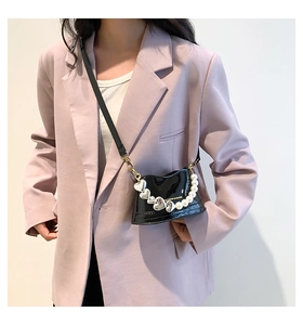 Detail of black patent leather bag featuring pearl and heart charm chain on purple blazer