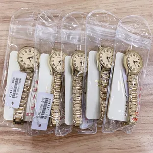 Detail view of five quartz watches with gold metal bands and Roman numeral dials on a wood desk