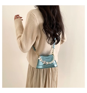 Back view of model wearing a mini metallic blue crossbody bag with pearl and heart chain detail