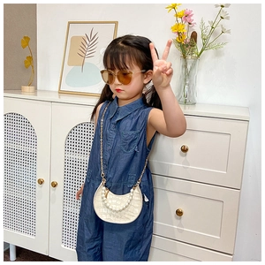 Detail of cream saddle bag with faux pearl handle and gold chain on denim dress