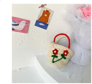 Detail of a handmade straw mini handbag with red crochet flowers and a red fabric handle