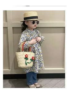 Detail display of a girls cream woven straw handbag featuring cute red flower decorations