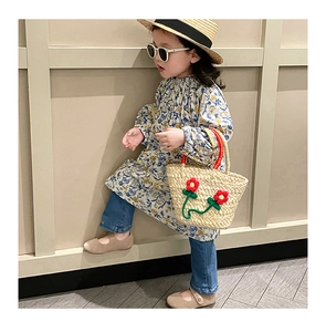 Detail of a girls floral dress paired with a woven straw bag and summer straw hat