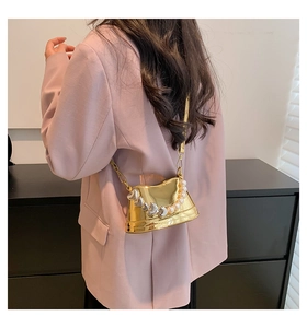 Dettaglio di una mini borsa a tracolla dorata con perle a cuore e catenina sottile