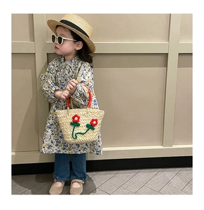 Kids woven straw bag with red handles and crochet flower accessory shown on a model