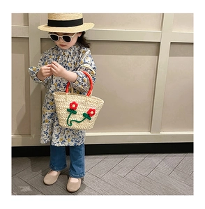 Detail of child wearing straw hat holding a woven beach bag with red 3D floral accents