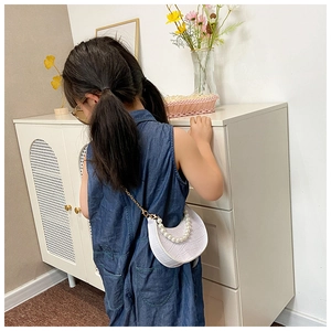 Rear view of a child wearing a white croc-embossed mini bag with pearl handle and gold chain