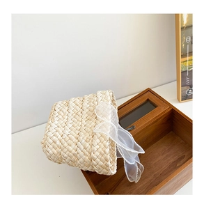 Detailed view of beige straw hat featuring elegant white lace bow in a rustic wooden box