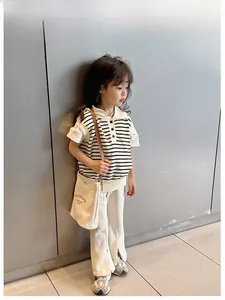 Gros plan d'un enfant en gilet rayé, pantalon large blanc et petit sac en toile décontracté