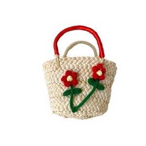Handwoven straw basket bag for girls featuring red crochet flowers and ribbon handles