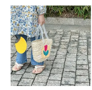 Detailed shot of children's straw bag with tulip embroidery and pearl mesh handle