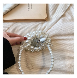 Close-up of handmade white pearl woven mini handbag with long pearl strap and glass bottle