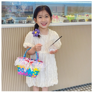 Close-up of a colorful woven bag with white lace trim, red bow, and strawberry charm