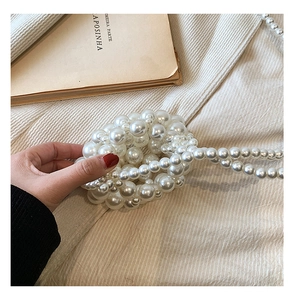Close-up of white imitation pearl woven handbag with beaded strap on a soft knit fabric