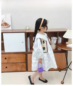 Dettaglio di abito bianco a maniche lunghe con gilet all'uncinetto a fiori da bambina