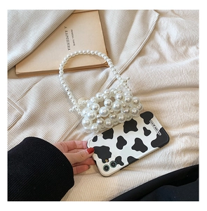Detail of handmade pearl woven mini handbag paired with cow print phone case on fabric