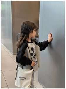 Détail d'un sac bandoulière en toile beige avec texte REDRIVER sur une tenue d'enfant