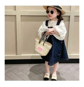 Detail of woven straw bag with floral pattern paired with denim dress for girls