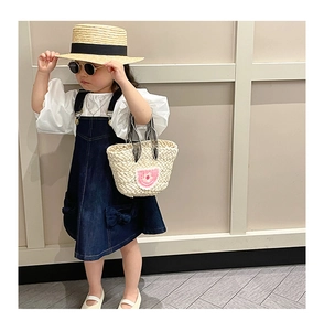 Detail of child floral woven handbag paired with denim dress and summer straw hat