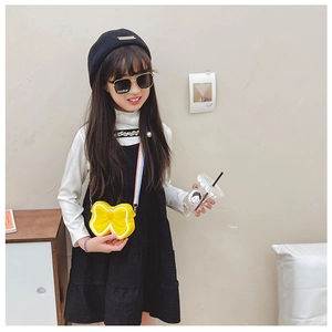 Toddler girl wearing a yellow bow silicone crossbody bag with rainbow strap on plain background
