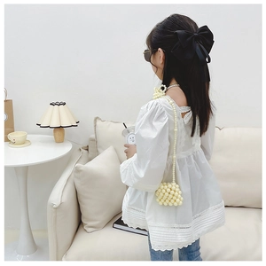 Dettaglio della camicetta di pizzo bianco per bambina con mini borsa di perle