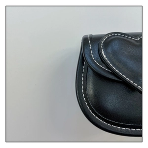 Détail macro du sac noir pour fille avec rabat en cœur et surpiqûres blanches contrastées