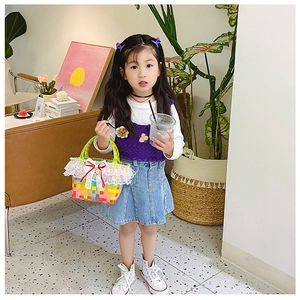 Detail of child hand carrying a colorful woven beach bag with lace and red ribbon bow