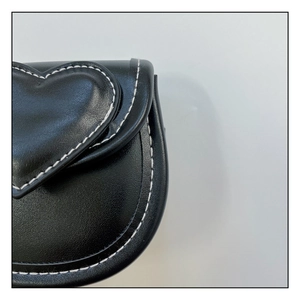 Détail macro d'un sac à bandoulière noir en forme de cœur avec surpiqûres blanches