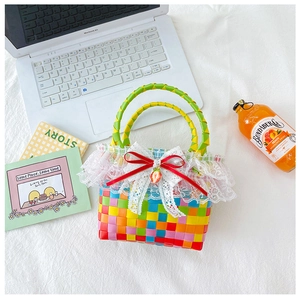 Detail of colorful woven handbag with white lace trim and strawberry pendant on a white fabric