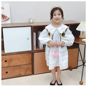 Dettaglio ricamo su gilet floreale vintage e abito in cotone bianco per bambina elegante
