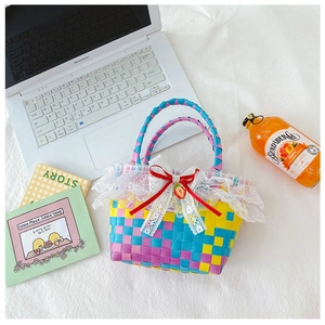 Detail of colorful woven girl's handbag with lace trim, red bow and strawberry charm