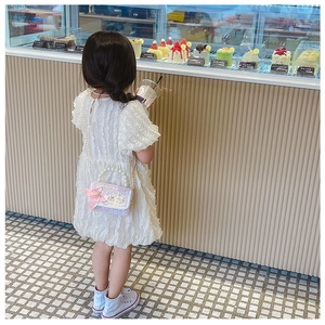 Fillette en robe blanche avec un sac à main à paillettes lilas et anse en perles