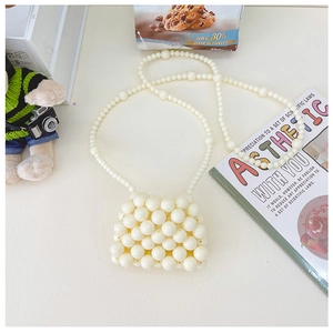 Dettaglio mini borsa in perle crema intrecciate con tracolla a catena lunga e manico