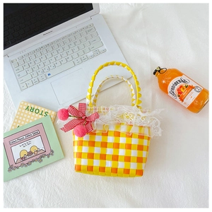Detail of yellow checkered woven bag with lace trim and cherry charm for summer picnic