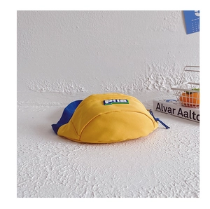 Détail du sac banane en toile jaune et bleu avec écusson logo sur fond texturé élégant
