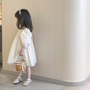 Fille en robe en dentelle crème avec un sac en paille à anse en perles sur fond blanc