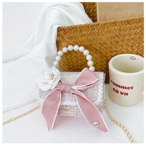 Detail of pink tweed girl bag with pearl handle, large bow, and white flower charm
