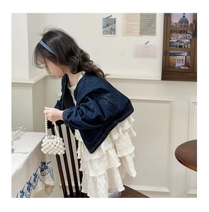 Dettaglio giacca di jeans e abito bianco a balze per bambina con borsa di perle