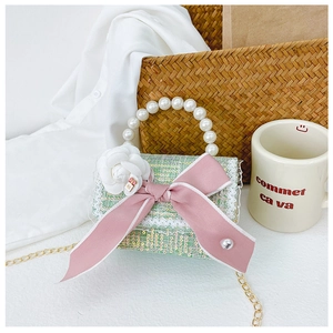 Detail of green tweed mini bag with pearl handle and pink bow on a lifestyle background
